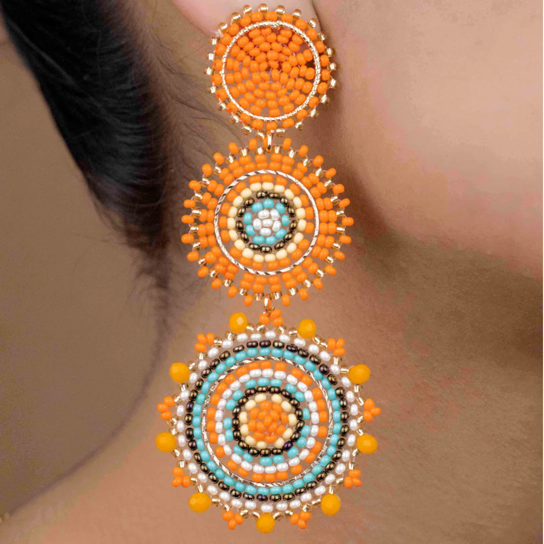 Ornate earrings with orange, blue, and gold beads on a blurred background