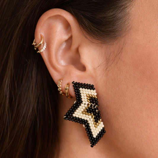 Close-up of an ear wearing a star-shaped beaded earring with gold and black details.