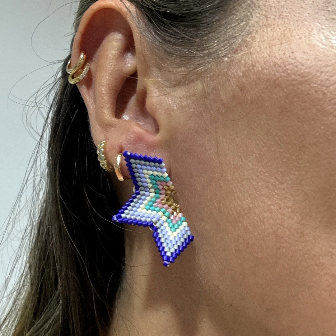 Close-up of an ear wearing a colorful beaded earring with additional earrings in the background.